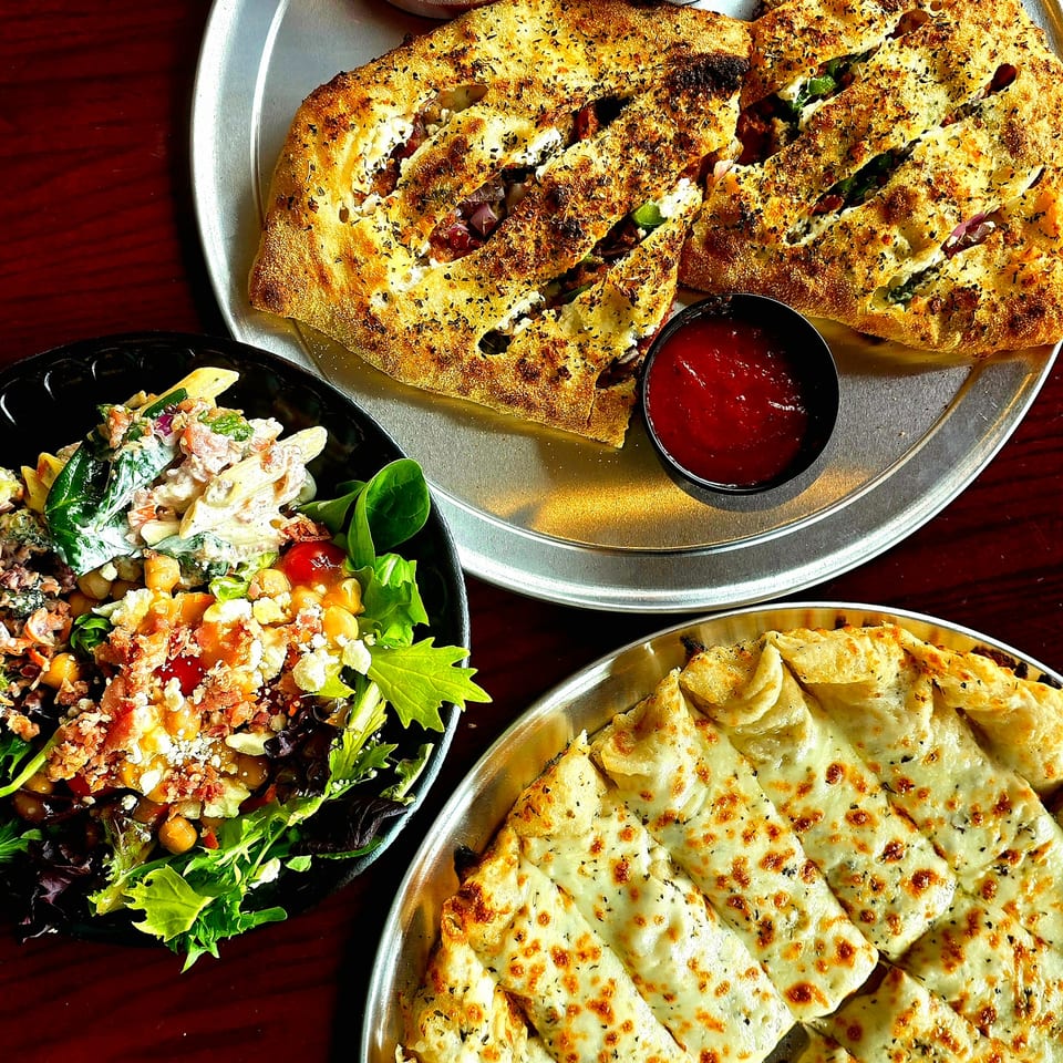 Overhead view of stuffed flatbreads, cheesy baked slices, fresh salad, and red dipping sauces on metal plates.