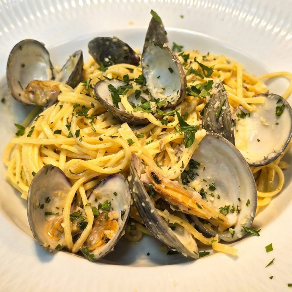 Creamy spaghetti topped with opened mussels and clams, garnished with chopped parsley on a white plate.