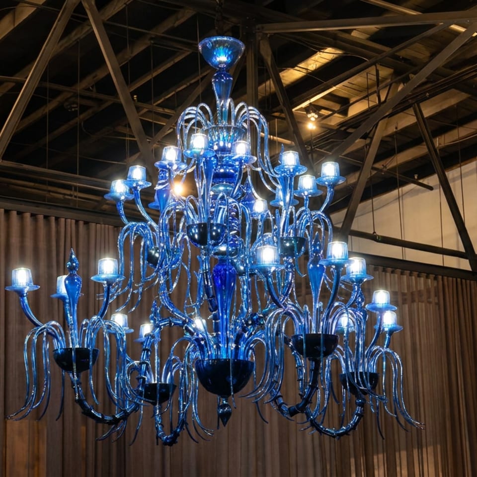 Large ornate blue glass chandelier with numerous glowing bulbs hangs beneath exposed wooden beams in a restaurant interior.