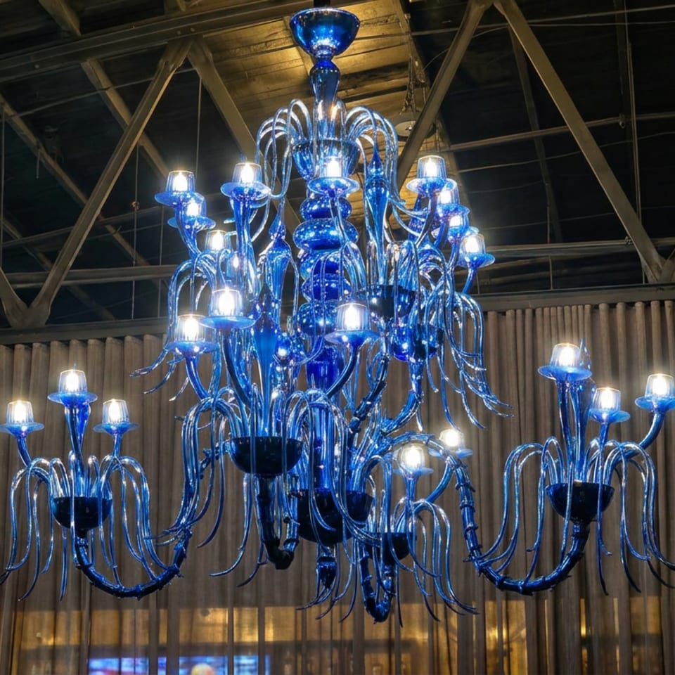 Ornate blue glass chandelier glowing inside a rustic restaurant with exposed beams and corrugated metal walls.