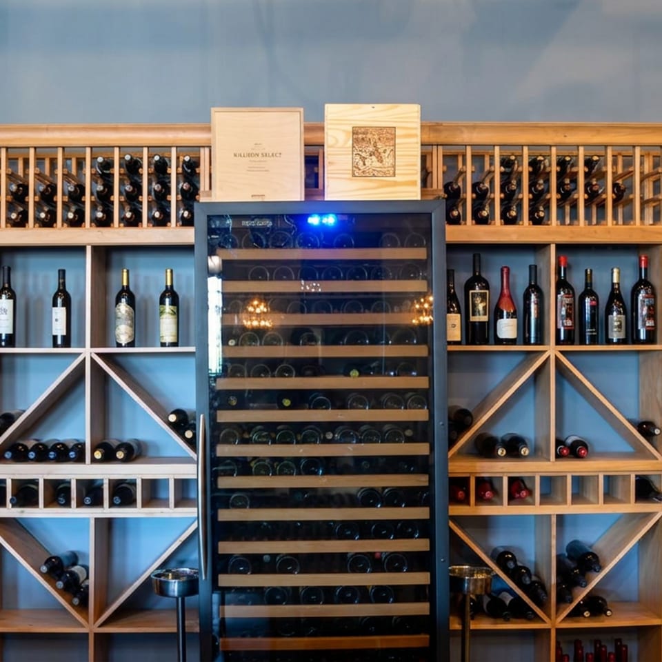 Wall-to-wall wooden wine racks display hundreds of bottles around a central glass-fronted wine cabinet.