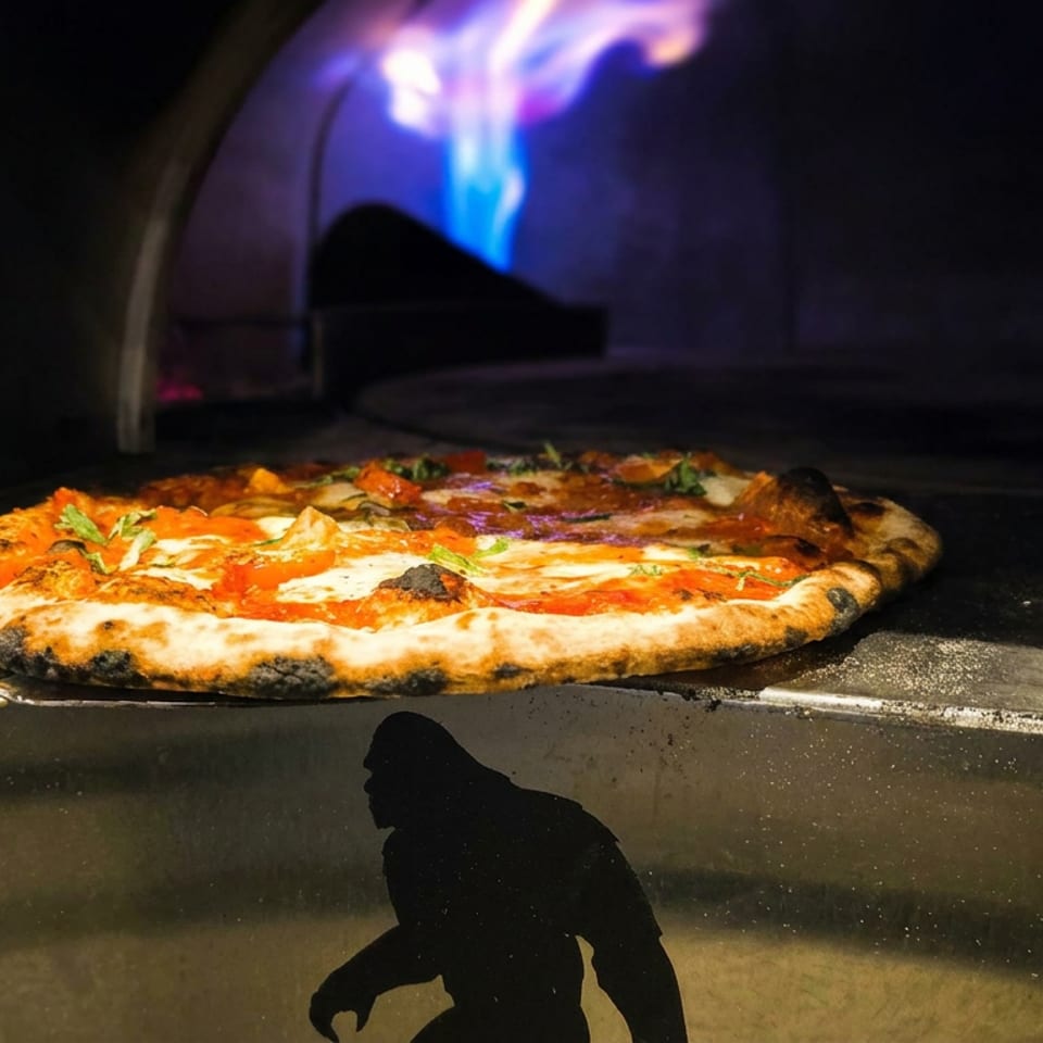 Freshly baked wood-fired pizza with blistered crust rests on a metal peel inside a glowing oven.