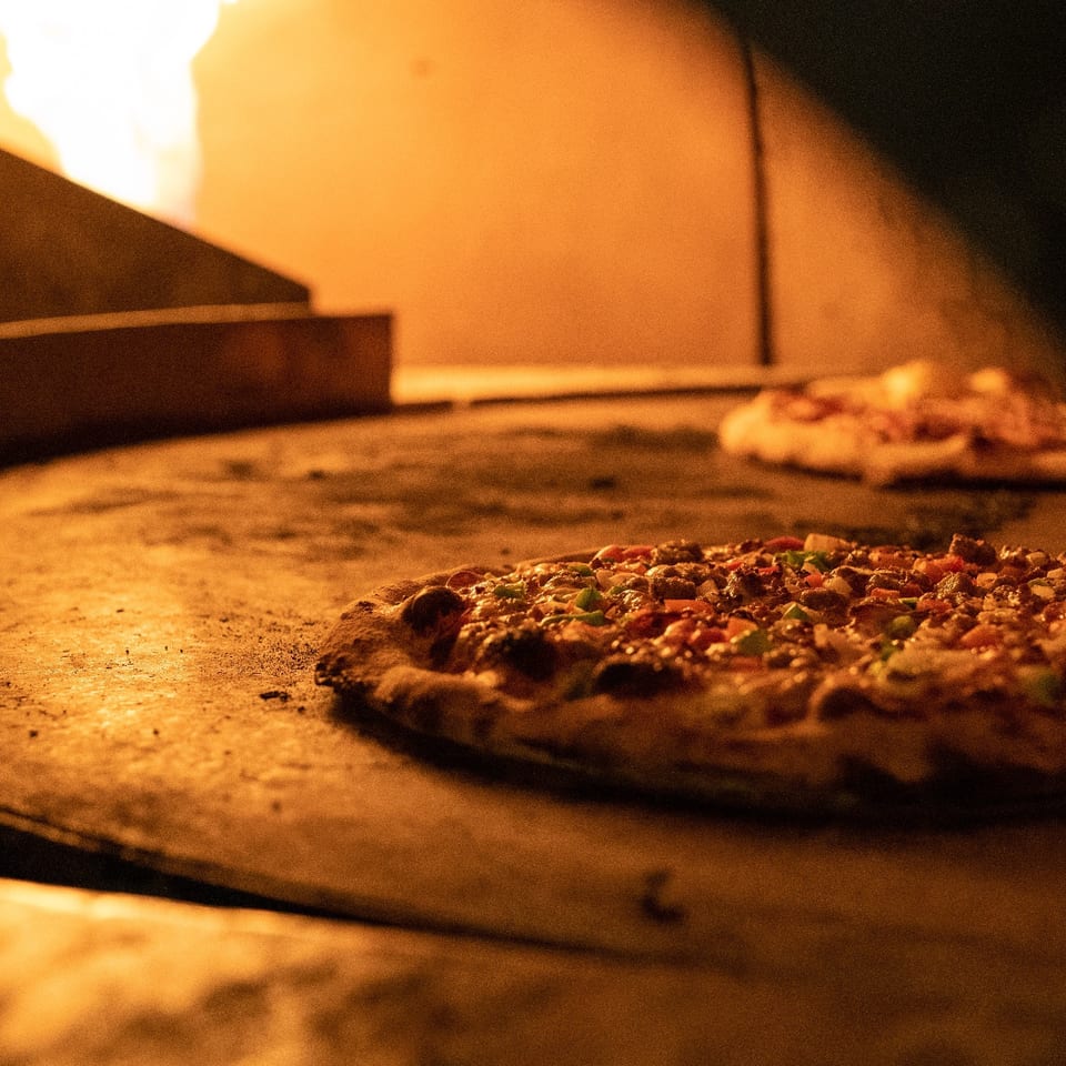 Pizzas baking inside a warmly lit wood-fired oven.