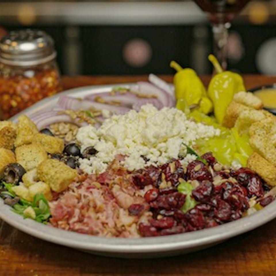 Large platter of colorful rice, grains, herbs, pickled vegetables, olives, and crispy toppings with dipping sauces on a wooden table.