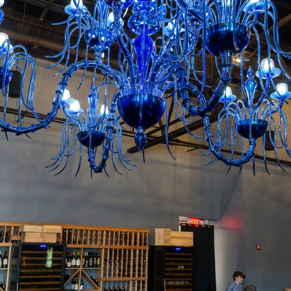 Ornate blue glass chandelier illuminates a modern restaurant with extensive wooden wine racks and seated diners.